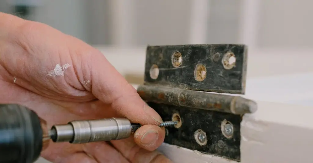 Unrecognizable professional male carpenter using screwdriver to attach metal hinge on window in room with blurred background during renovation works